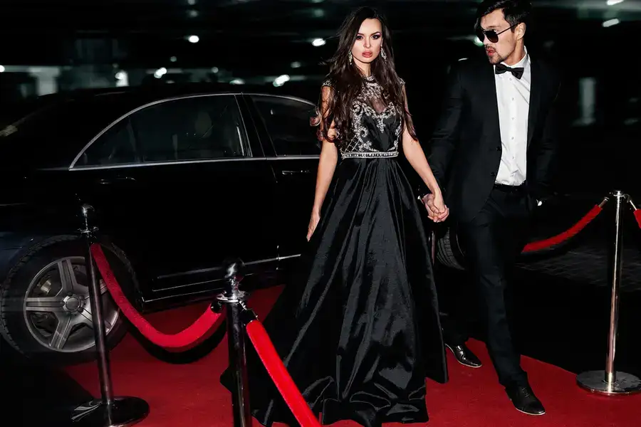 Sexy Couple Use the Black Car Service. Hollywood star. Fashionable pair of elegant people at night city street.